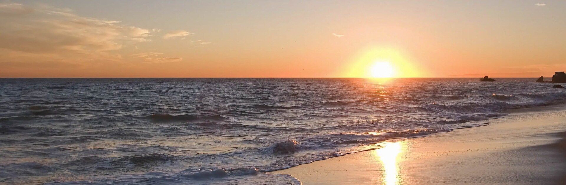 A golden sunset over the ocean, waves rolling onto the sand off Huntington Harbour